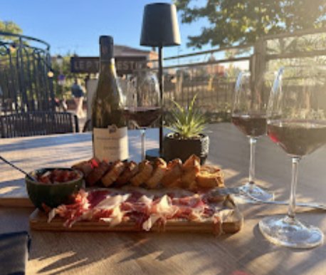Planche de charcuterie et verres de vin sur une table en bois, en terrasse au soleil couchant.