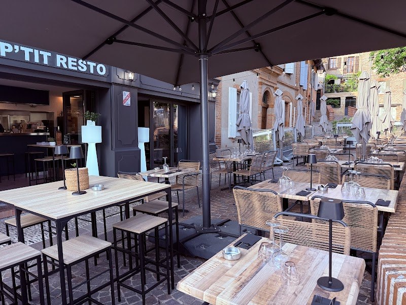 La terrasse du P’tit Resto sous le grand parasol, tables en bois et chaises en rotin sur les pavés de la place du Château.